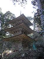 A three-storied wooden pagoda in a forest.