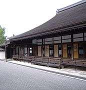 A wooden building with roofed veranda next to a raked gravel garden.
