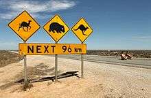 Warning signs stand out as the only feature alongside a road through a flat, treeless, landscape