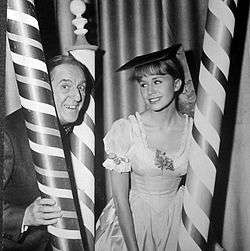 publicity shot of elderly man and young female sitting between three poles