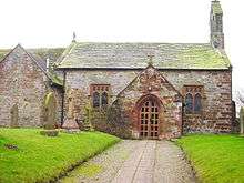 Part of a simple, small church seen from the north, with a projecting porch and vestry and a bellcote on the west gable