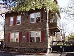 A brown 2 1/2 story house with red shutters.