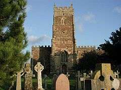 Square stone tower behind churchyard with cross and gravestones.