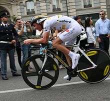 A cyclist wearing a white skinsuit while riding a bike.