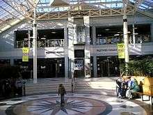 two storey silver clad building set behind an internal glazed square with circular floor feature