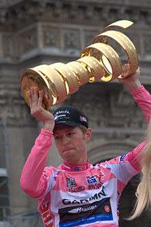 A man wearing a pink jersey while holding a golden trophy.
