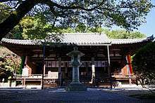 Wooden building with hip-and-gable roof, slightly raised floor, white walls and an open railed veranda.