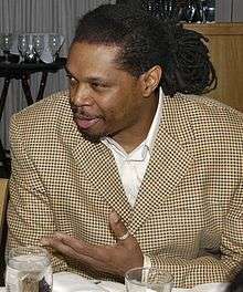 A middle-aged man, wearing a brown suit, is sitting behind a dinner table.