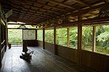 Room with wooden floor open on two sides. There is a small statue placed in the center of the room.