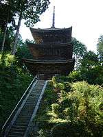 Wooden three-storied pagoda at the top of a long flight of stairs.