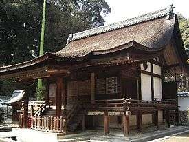 Wooden building with an asymmetric gabled roof and a raised veranda with handrail.