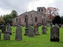 A broad stone church seen from the east with aisles of differing sizes and a battlemented west tower