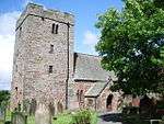 A stone church seen from the southwest with a massive west tower containing very small windows