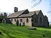 A stone church consisting of a nave, a chancel with aisles, each under a separate roof, a south porch, and a west bellcote.