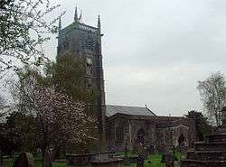 Stone building with square tower, partially obscured by trees.