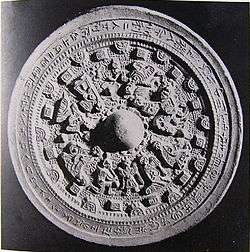 A round object with an inscription in Chinese characters around the outer part and figurative relief in the middle.