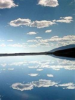 A slightly cloudy blue sky view across the blue waters of Summit Lake