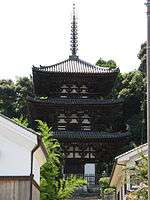 Wooden three-storied pagoda with white walls and dark beams.