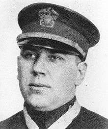 Head of a young man with full cheeks wearing a military peaked cap and looking off into the distance.