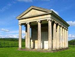 Stone building with pillars, surrounded by grass.