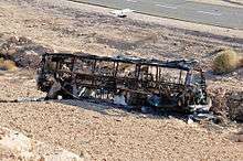 Black frame of a bus lying on gravel ground to the side of a highway road