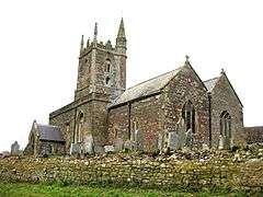 Stone church view from a low angle. The church has a simple tower and there are gravestones in the churchyard surrounding it