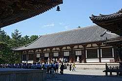 Wooden building with white walls and a hip-and-gable roof built on a stone platform.