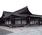 Wooden building with railed veranda, white walls and a hip-and-gable roof.