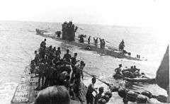 Three-quarter front view over the bow from the conning tower of another submarine with numerous people standing on both vessels