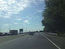 A four lane asphalt road with a grassy median approaching a traffic light. A green sign in the median reads Truck East 9 Truck East 404 left