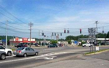 A signalized five-way intersection of three highways in an area composed of several commercial establishments.