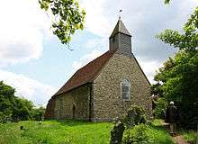 A small simple stone church with a red tiled roof and a wooden bellcote