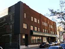 A three-storey brown-bricked building is shown from the street. On its ground floor is a National Car Rental agency, with a green awning over its offices.