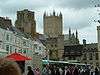 People at coloured market stalls. Surrounding are houses with the towers of the cathedral visible behind.