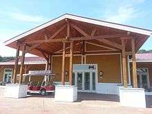 A large wooden building with a red roof, three wooden posts, with an electric golf cart parked in front.