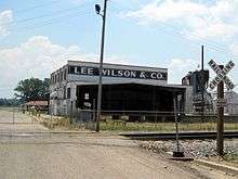 Abandoned white steel building with "Lee Wilson & Co" painted on top with railroad tracks in the foreground