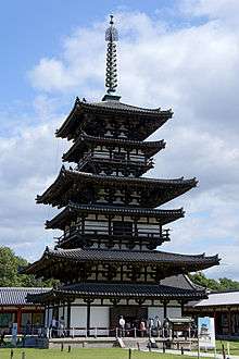 Three storied wooden pagoda with white walls. Additional pent roofs on every floor give the appearance of twice as many floors, i.e. six floors.