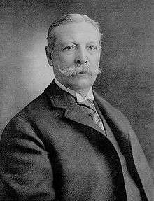 Portrait of Charles Yerkes wearing a frock coat, wing collar shirt and with a large handlebar moustache.